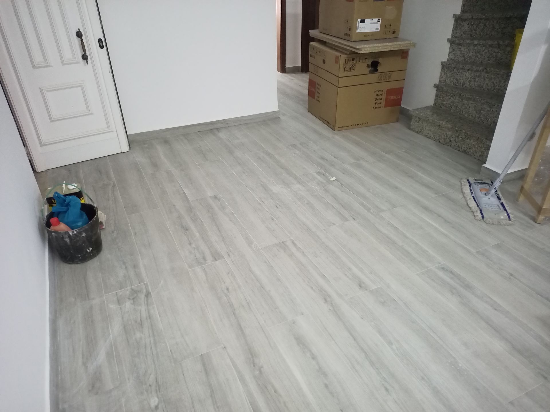 Piso de cerâmica imitando madeira em tom cinza claro em um cômodo com porta branca, armários embutidos e escada.