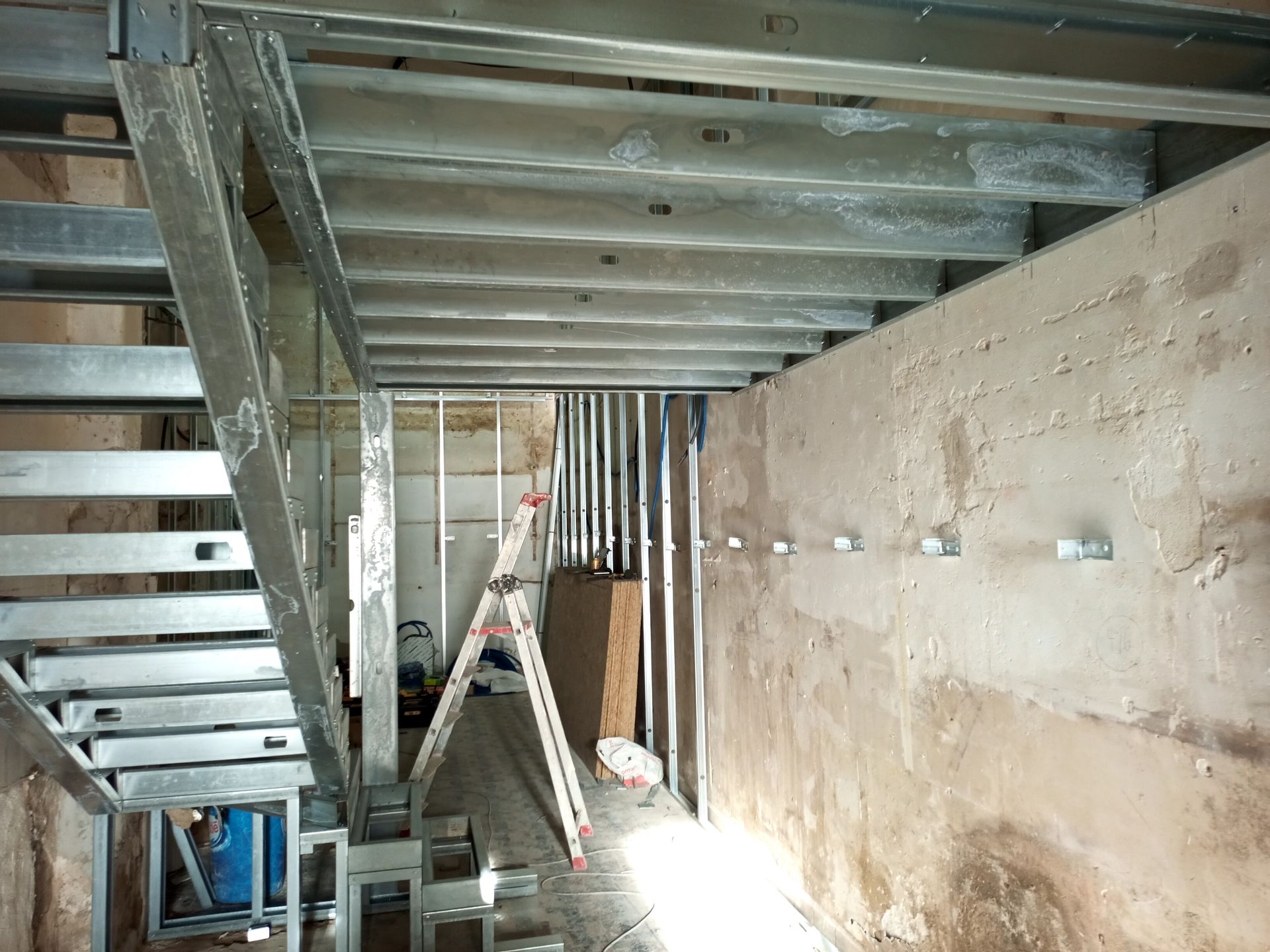 Canteiro de obras com estrutura metálica de escada e paredes inacabadas.
