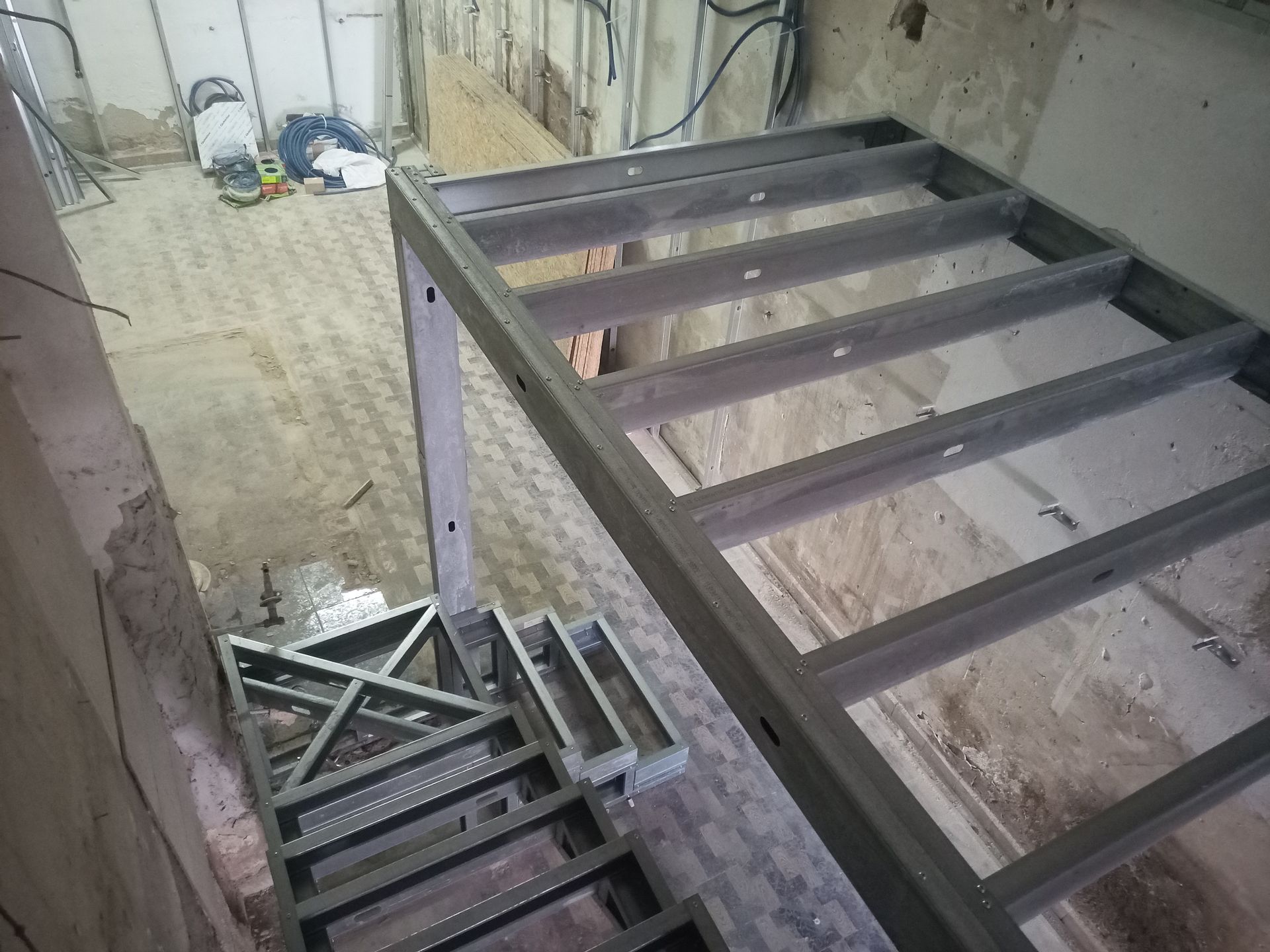 Estrutura metálica de escada em construção dentro de um edifício; paredes de concreto inacabadas.