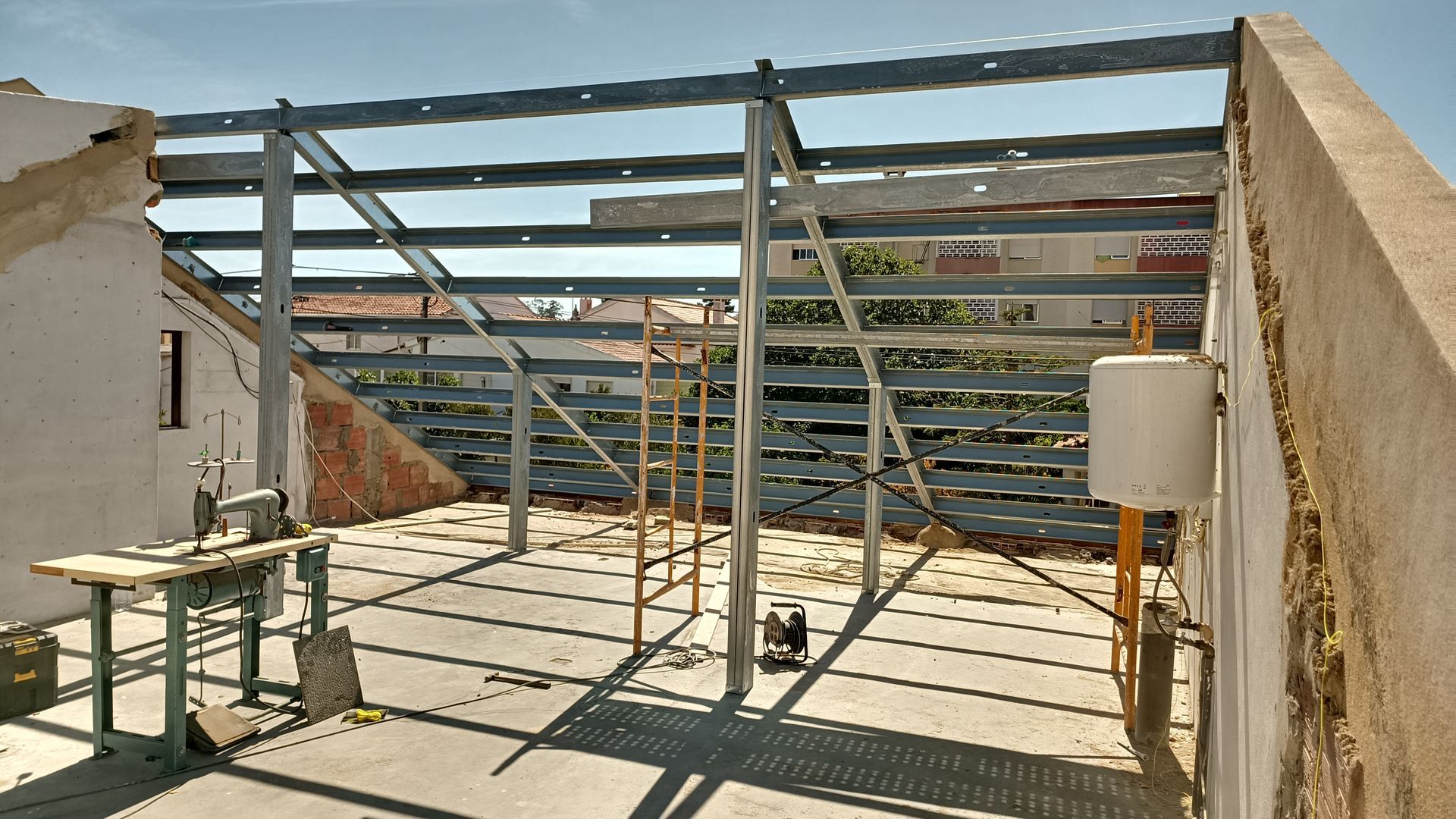 Estrutura metálica para cobertura, parcialmente construída com ferramentas e equipamentos sobre a superfície de concreto.