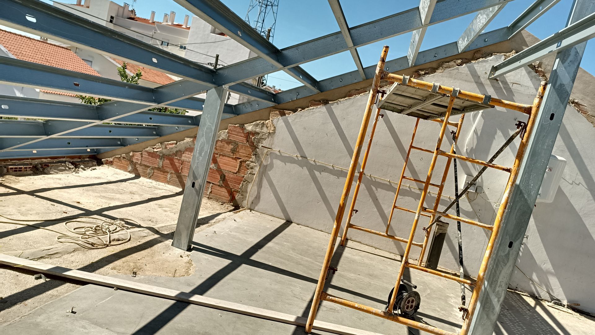 Canteiro de obras: vigas de aço, andaimes, parede de tijolos aparentes.