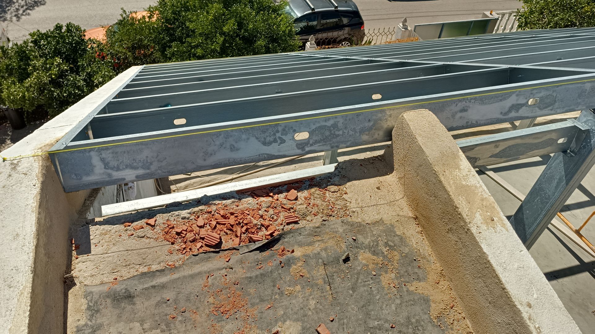 Vigas metálicas sendo instaladas em um telhado de concreto, com um veículo ao fundo.