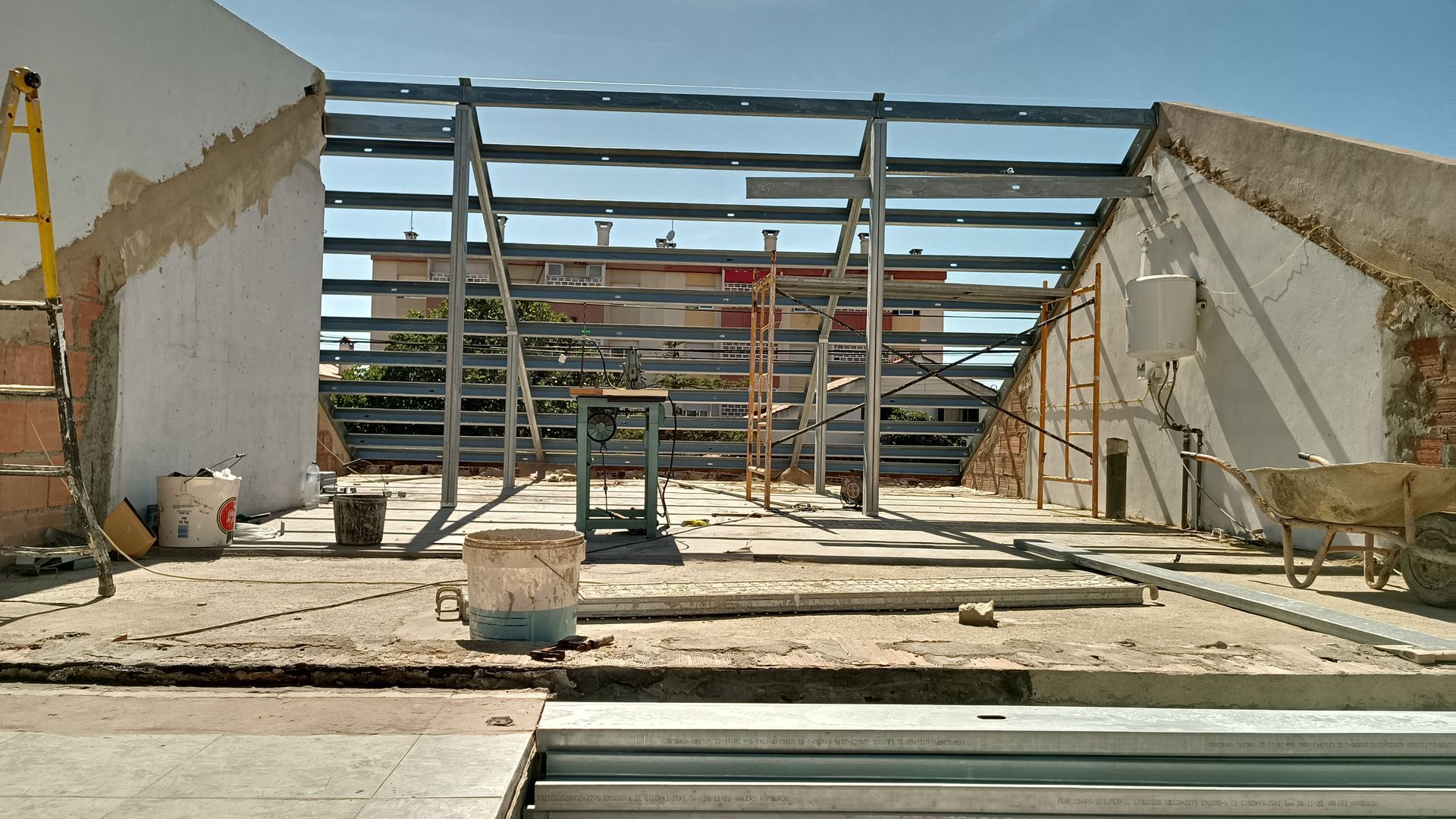 Canteiro de obras: estrutura metálica instalada entre paredes; materiais espalhados pelo chão.