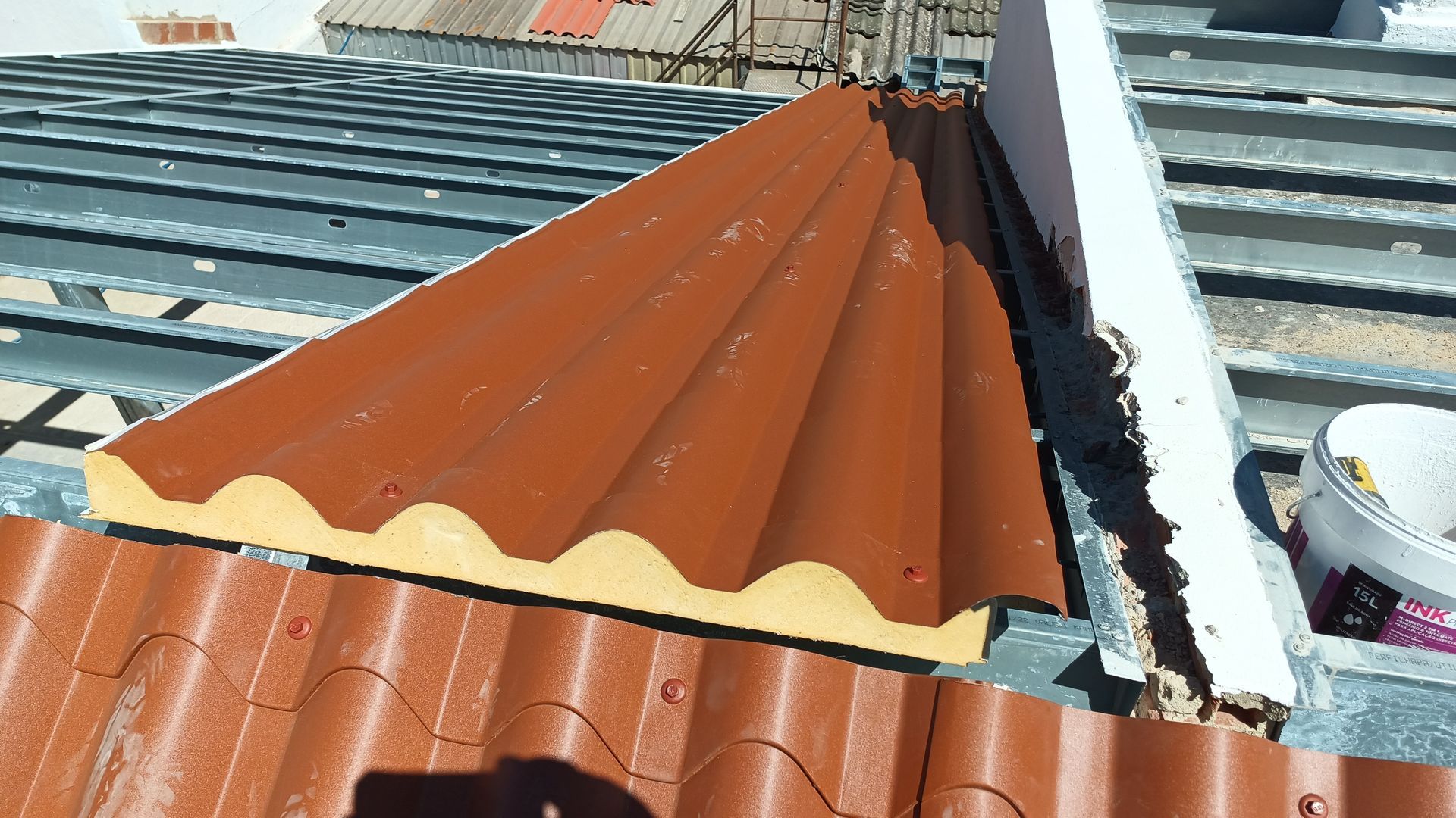 Painel de telhado ondulado marrom sendo instalado em um telhado com vigas metálicas.