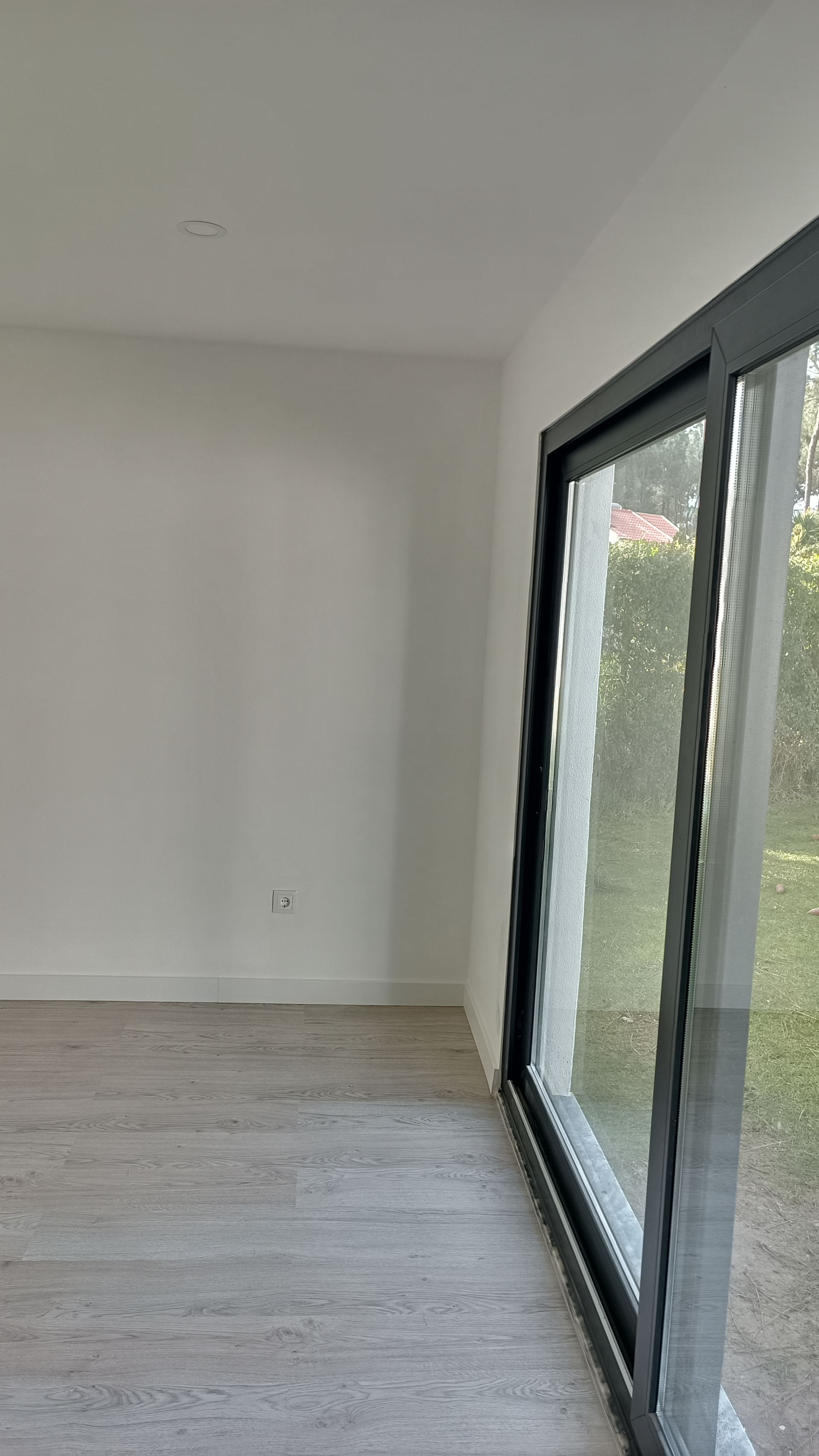 Interior de um quarto com paredes brancas, porta de vidro deslizante e piso que imita madeira.