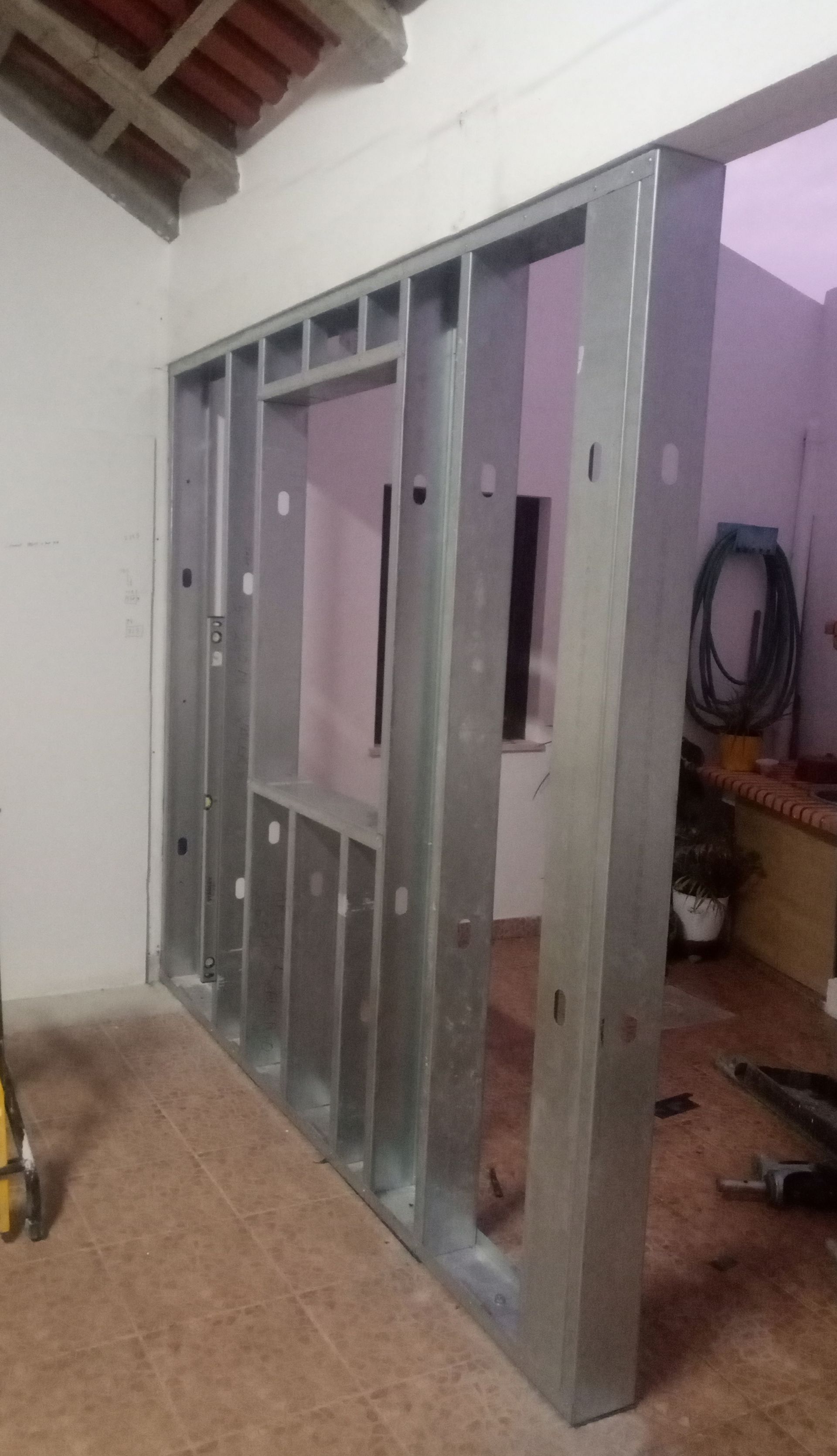 Estrutura de parede com montantes metálicos, com abertura para janela/nicho, em um cômodo com piso de concreto.