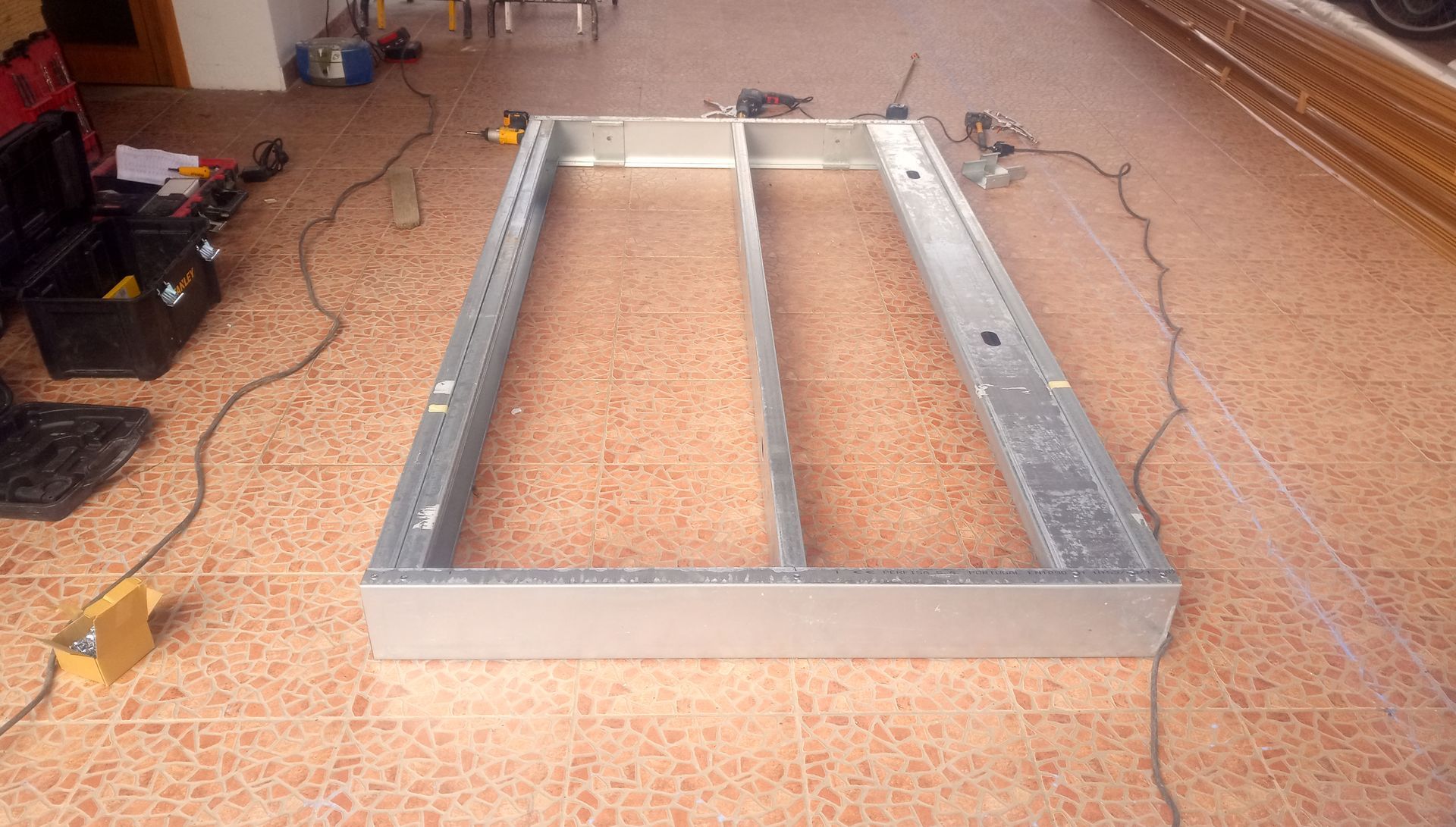 Estrutura metálica sobre piso de azulejo, possivelmente para um armário. Ferramentas e materiais estão próximos.