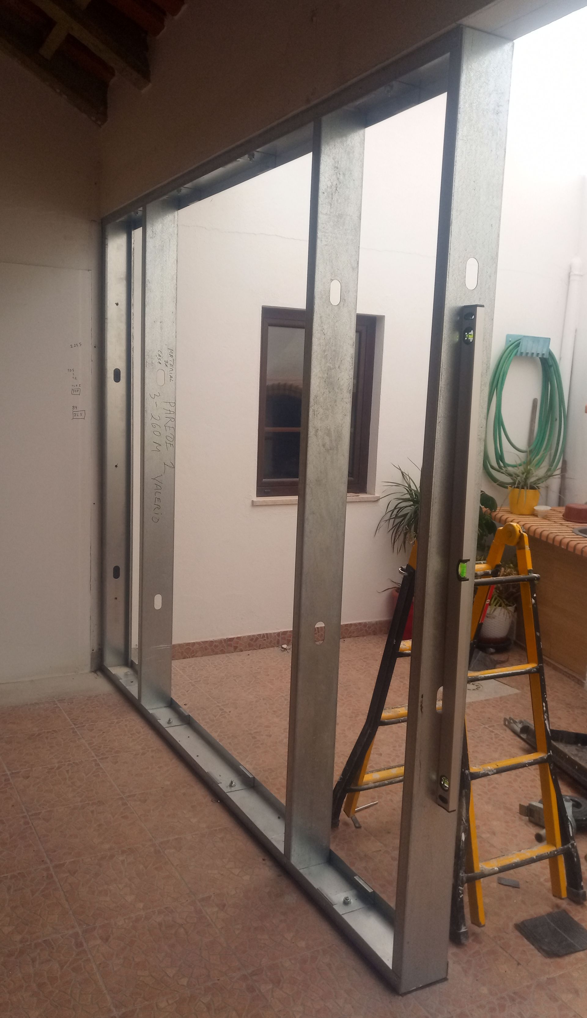 Estrutura metálica de uma parede, aberta para um pátio. Uma escada e uma mangueira estão próximas.