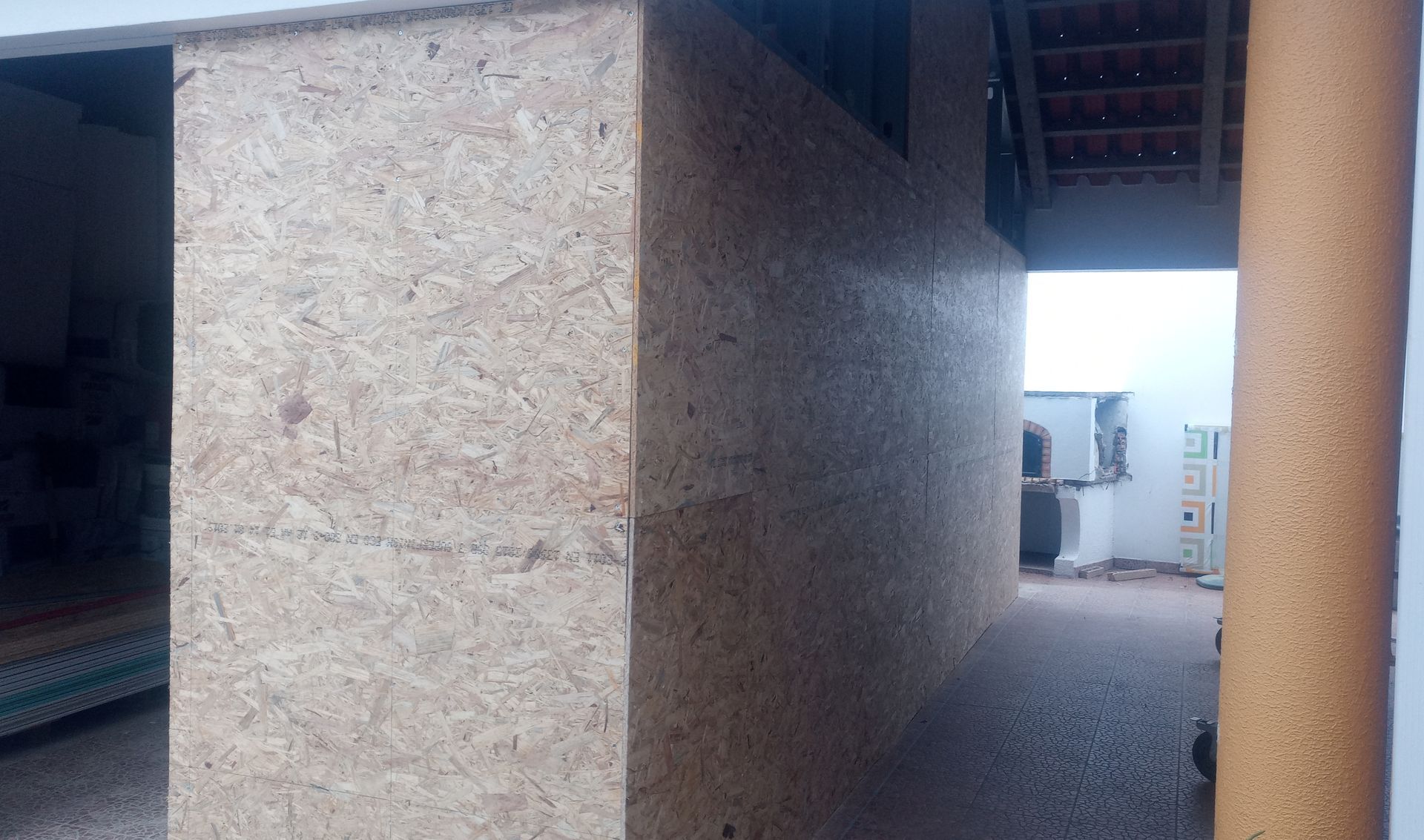 Paredes texturizadas em tom bege com abertura para uma área externa com estrutura branca e aparelho de ar condicionado.