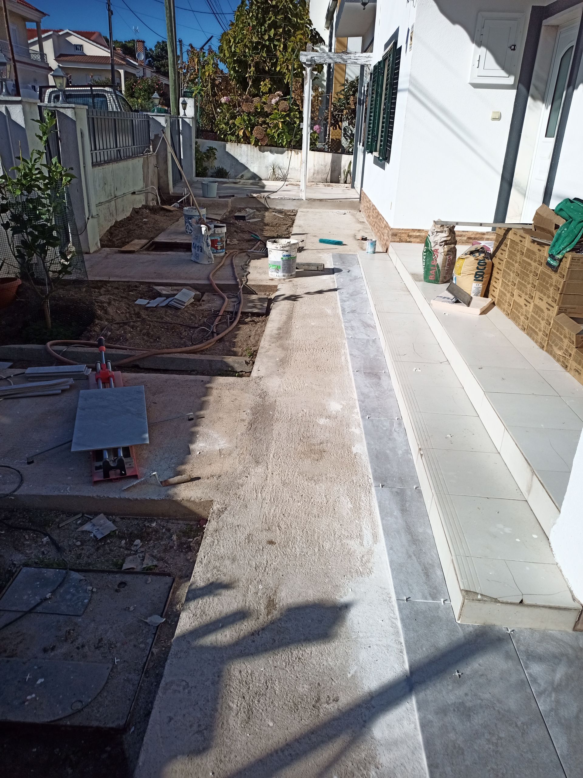 Caminho com bordadura de concreto e metal, em construção. Adjacente a um prédio branco.