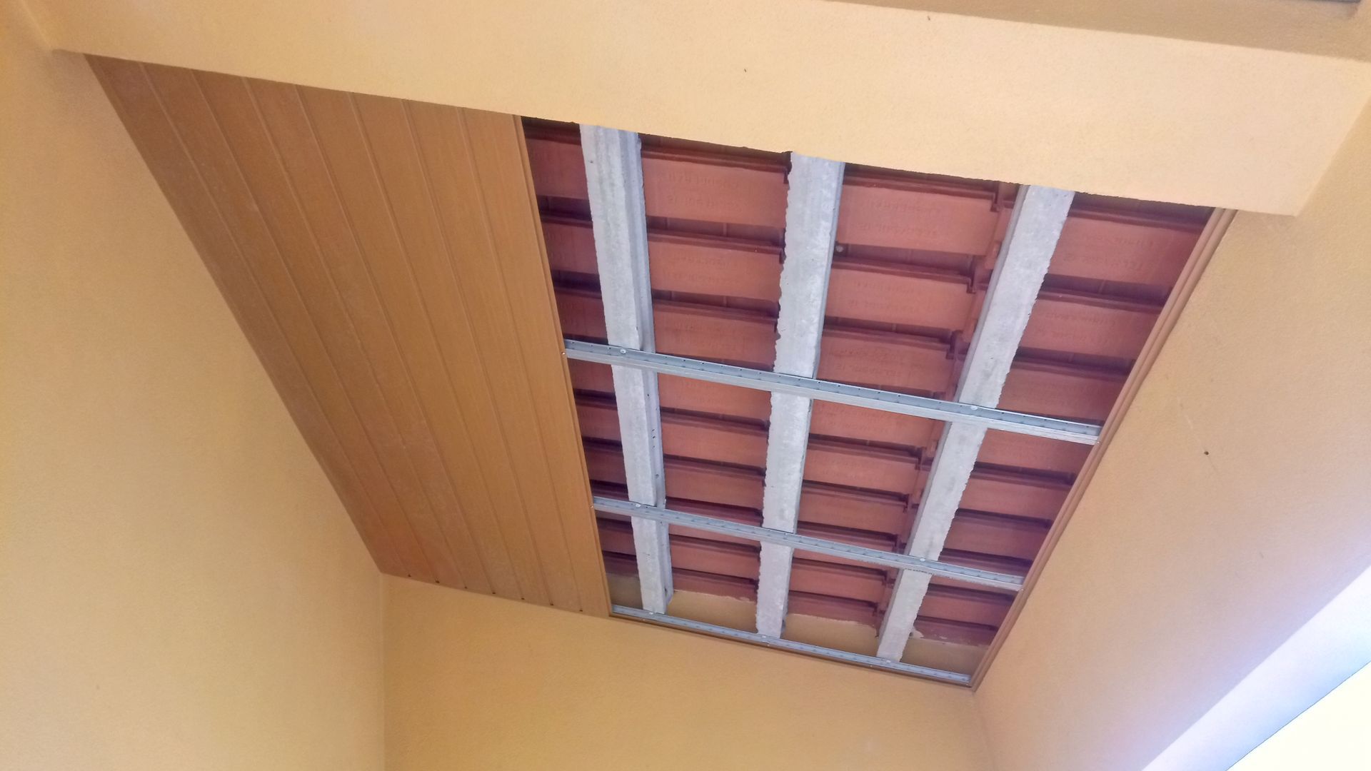 Teto parcialmente revestido com painéis de madeira, revelando a estrutura metálica e os ladrilhos de terracota.