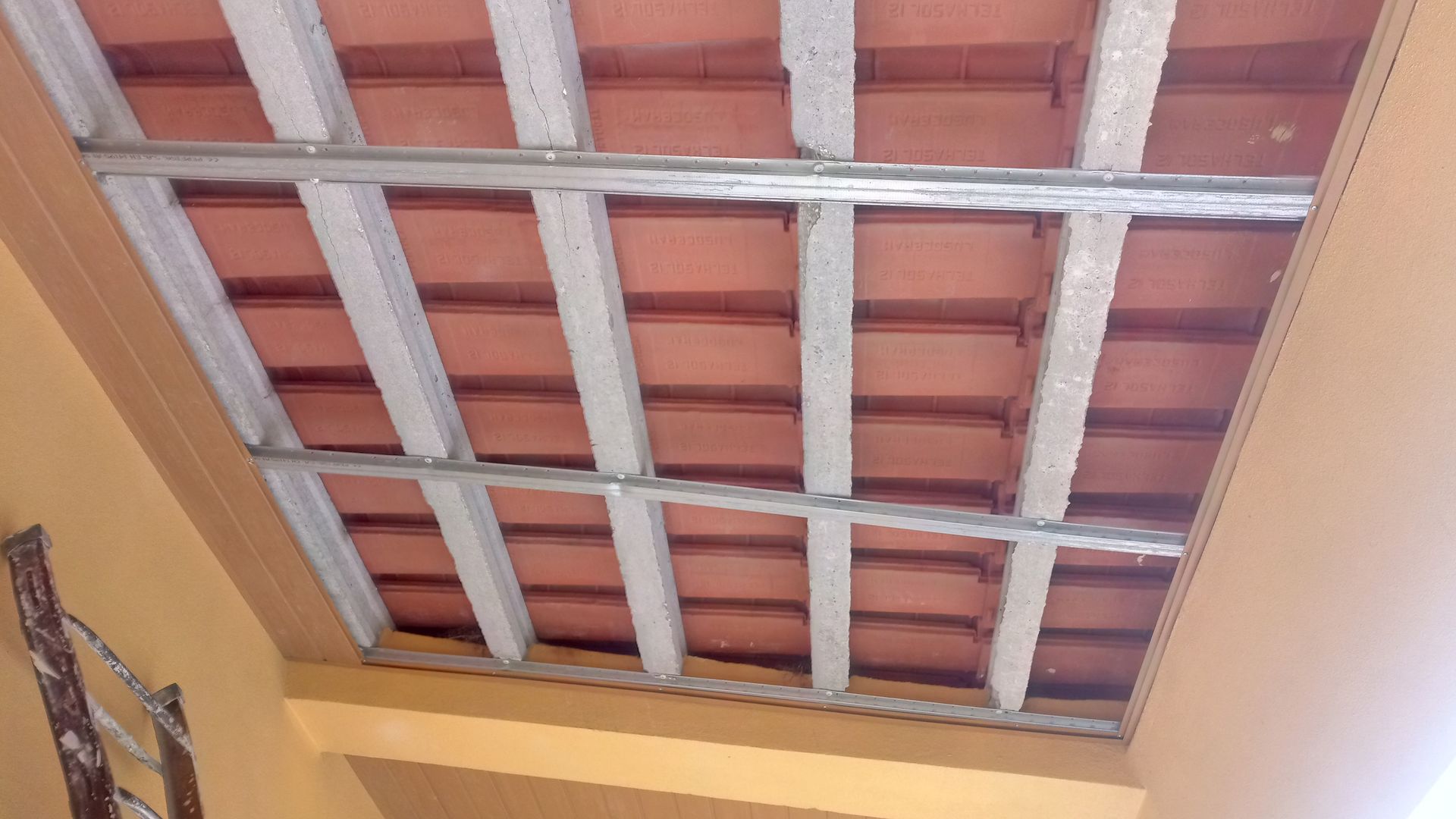 Vista de um teto com vigas de concreto e telhas de barro vermelho.