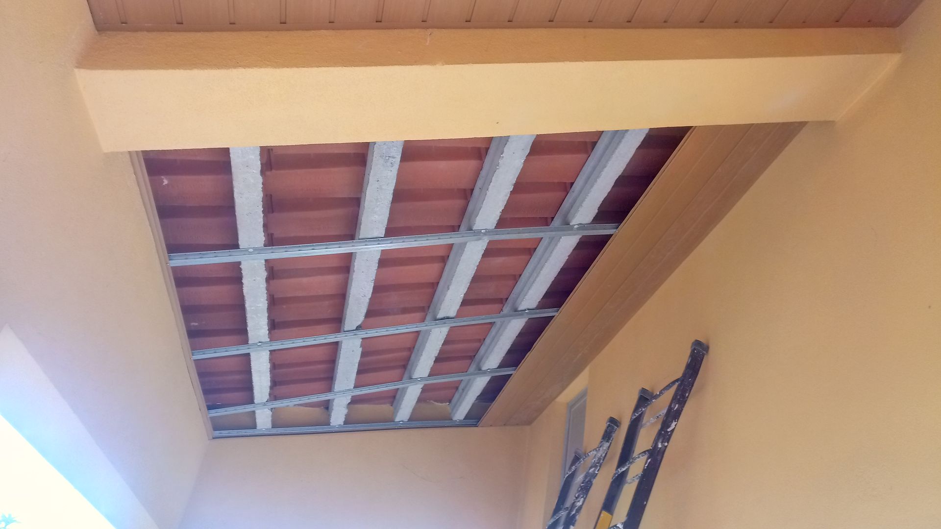 Fachada de prédio em estuque laranja com teto de tijolos aparentes e vigas de metal. Uma escada está encostada na parede.