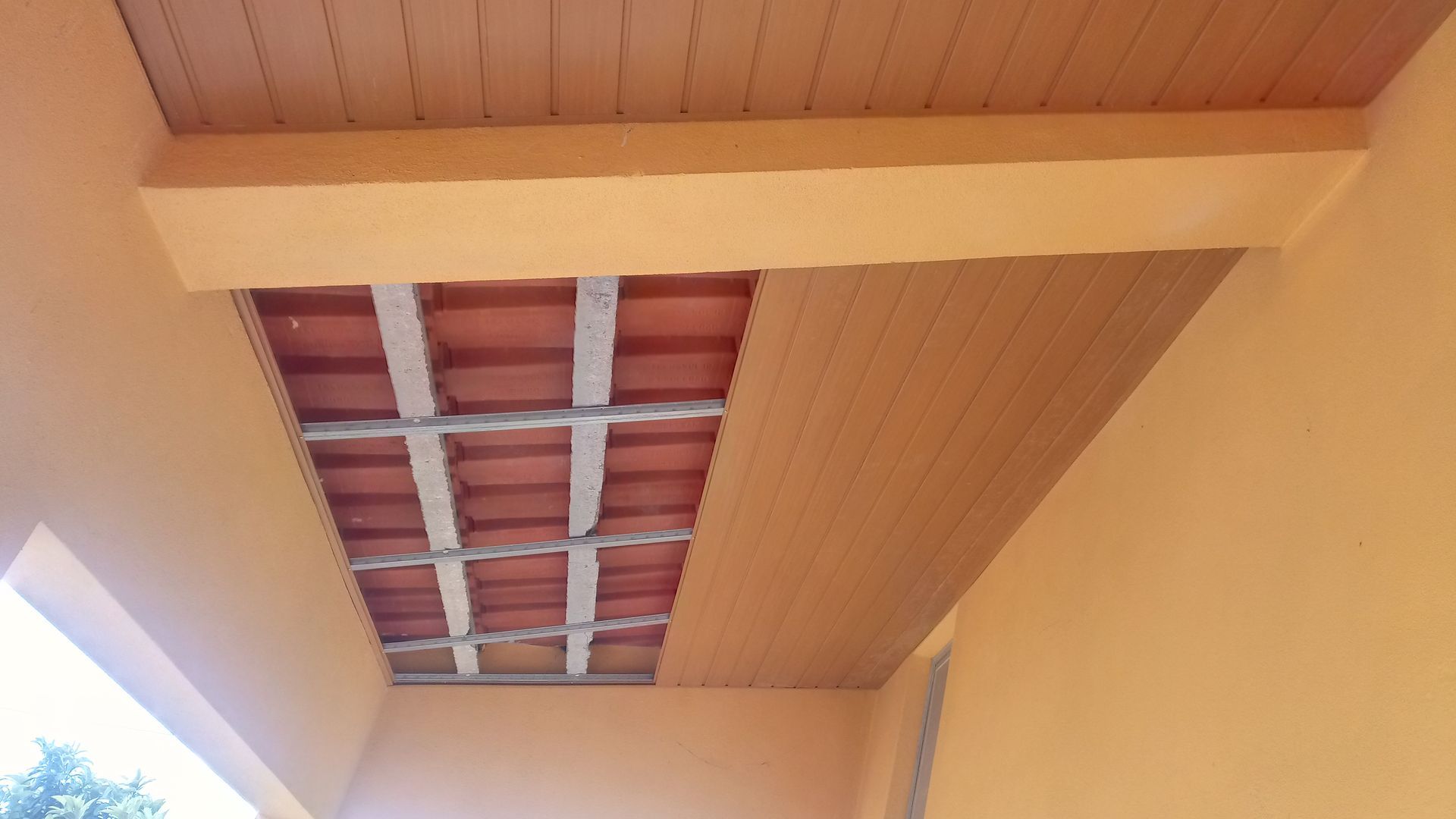 Teto exterior pintado de laranja com telhas de terracota e tábuas de madeira.