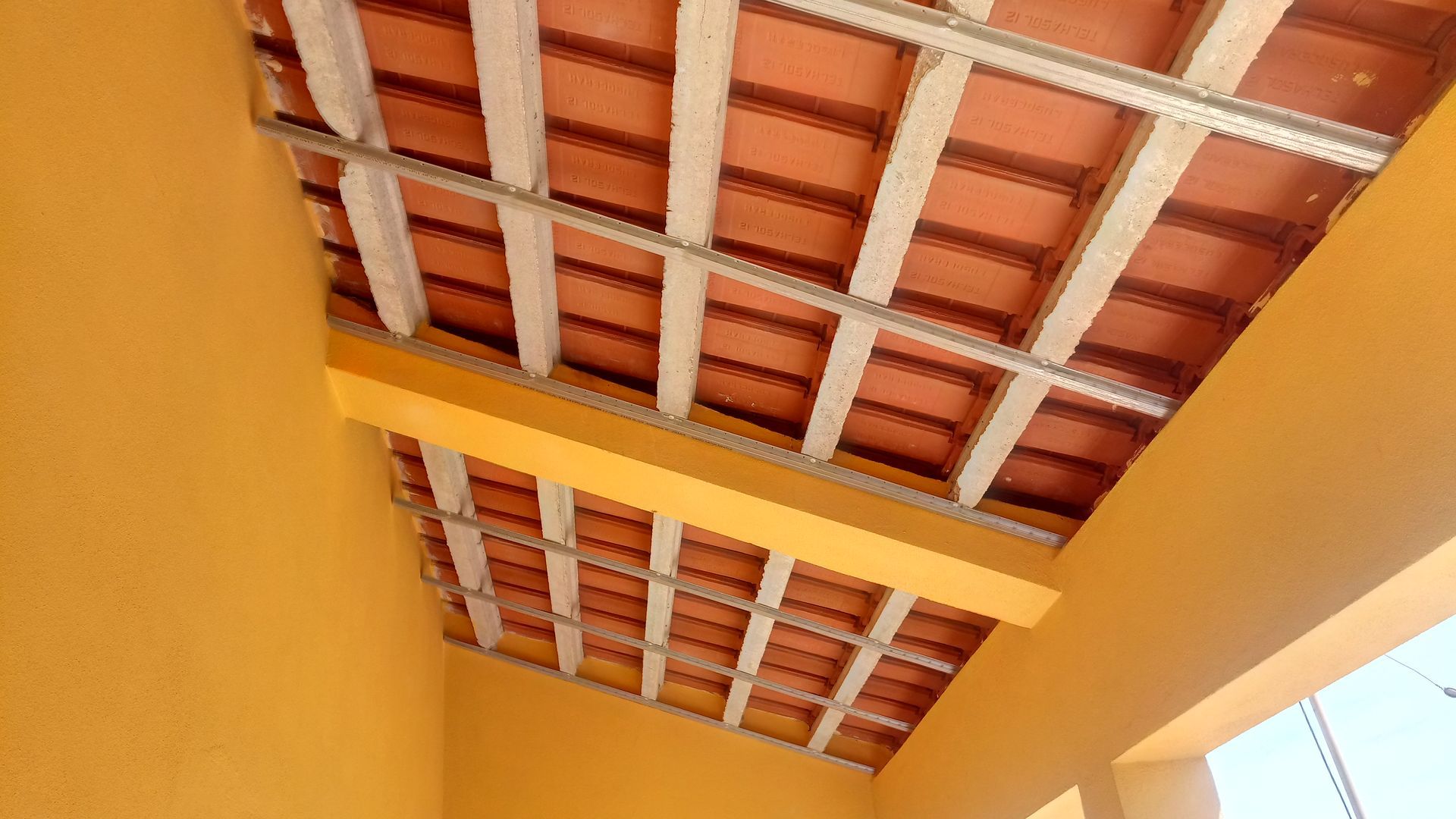 Exterior de edifício laranja com telhado de telhas sustentado por vigas brancas.