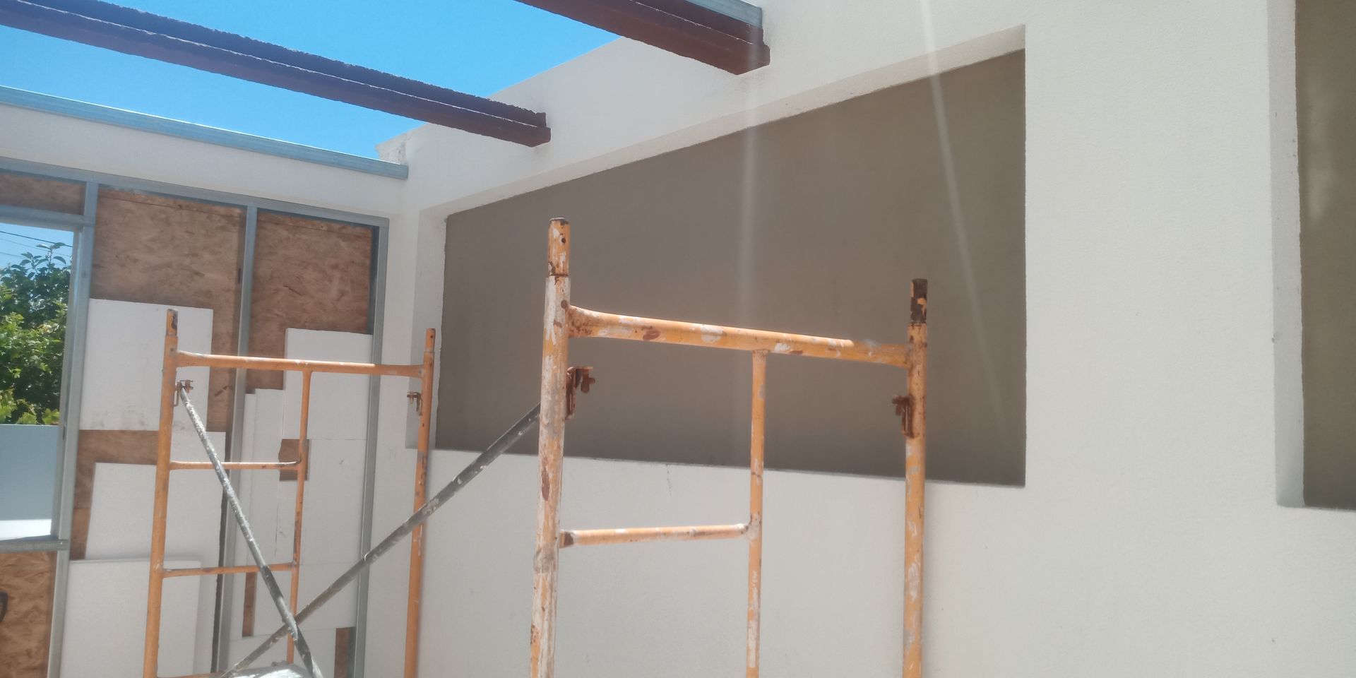 Canteiro de obras: andaimes junto a uma parede com uma grande janela, céu azul visível.
