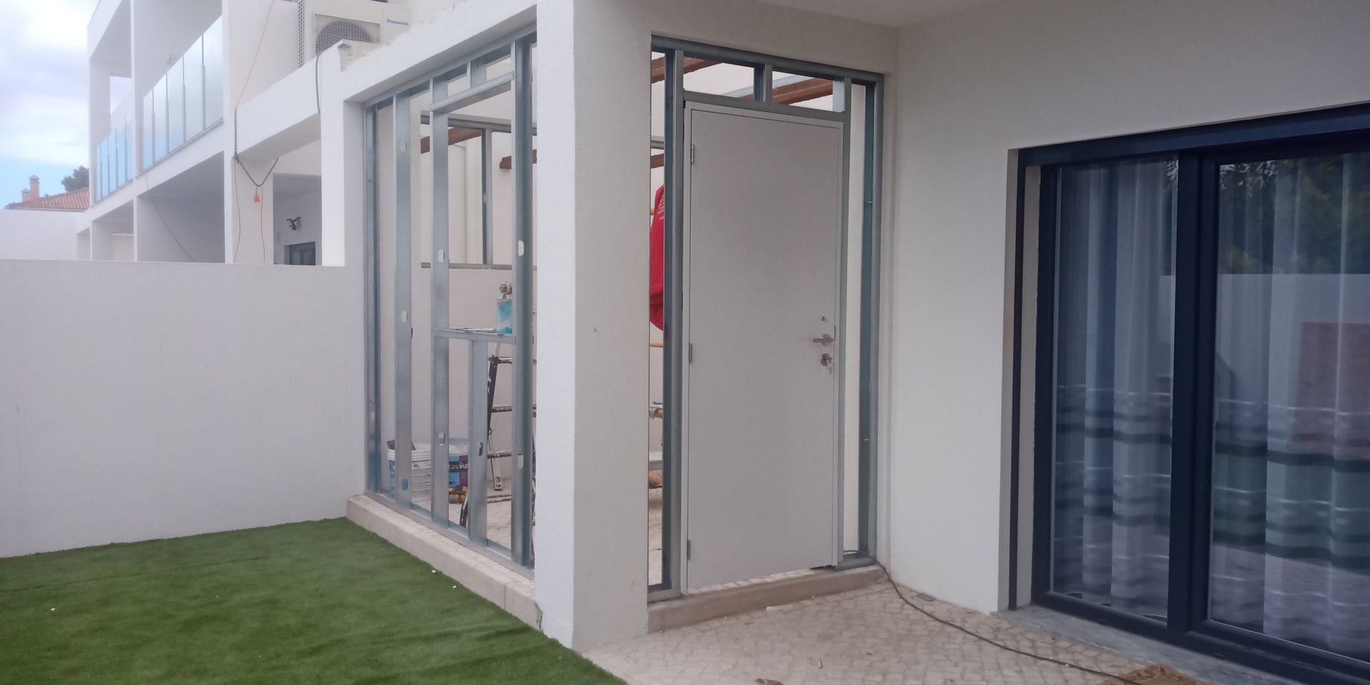 Exterior de um edifício moderno com porta e janela com vista para um pequeno jardim com grama artificial.