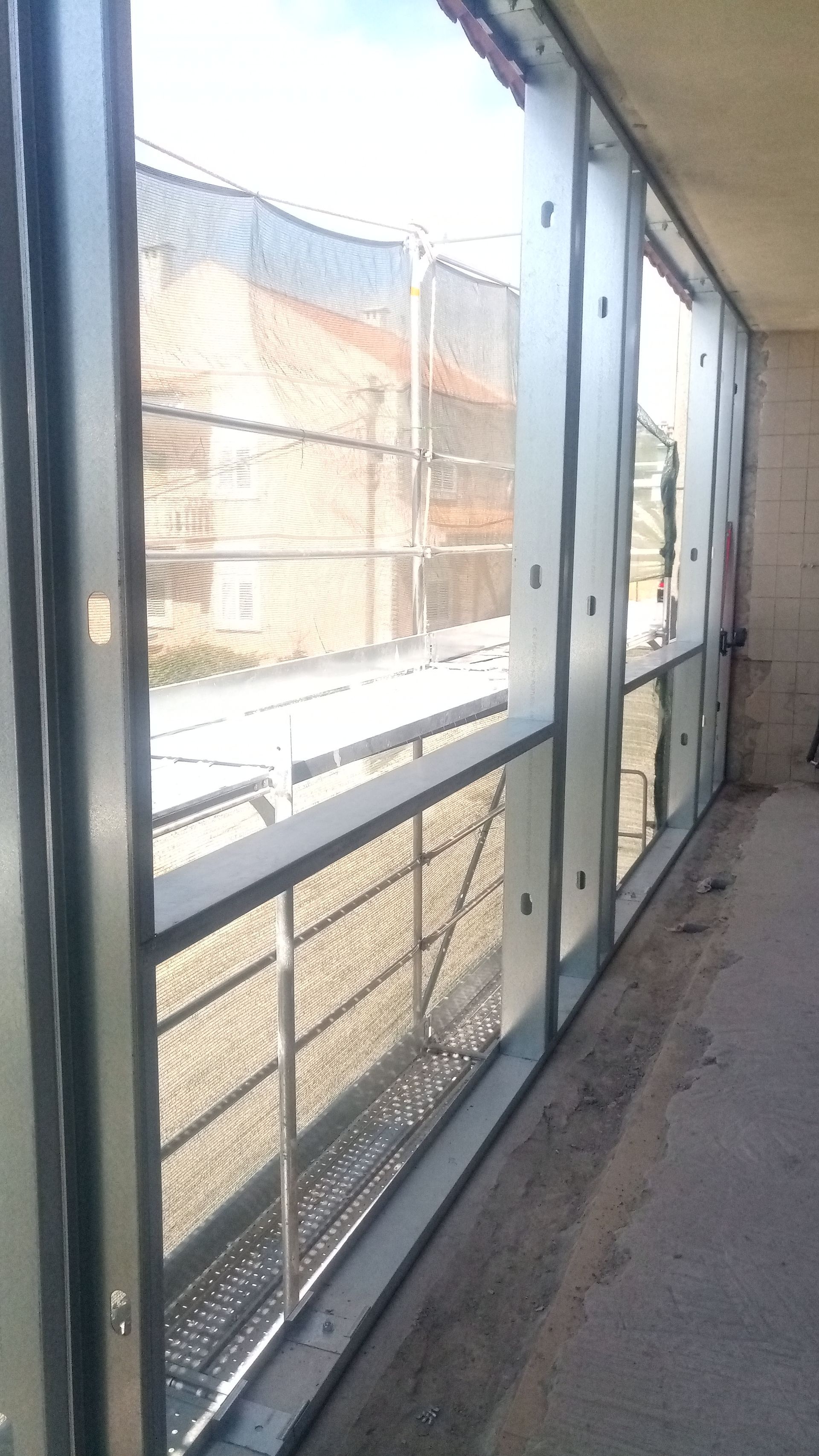 Janelas ao longo de uma parede de concreto com grades de segurança metálicas. Uma tela metálica se estende por toda a abertura.