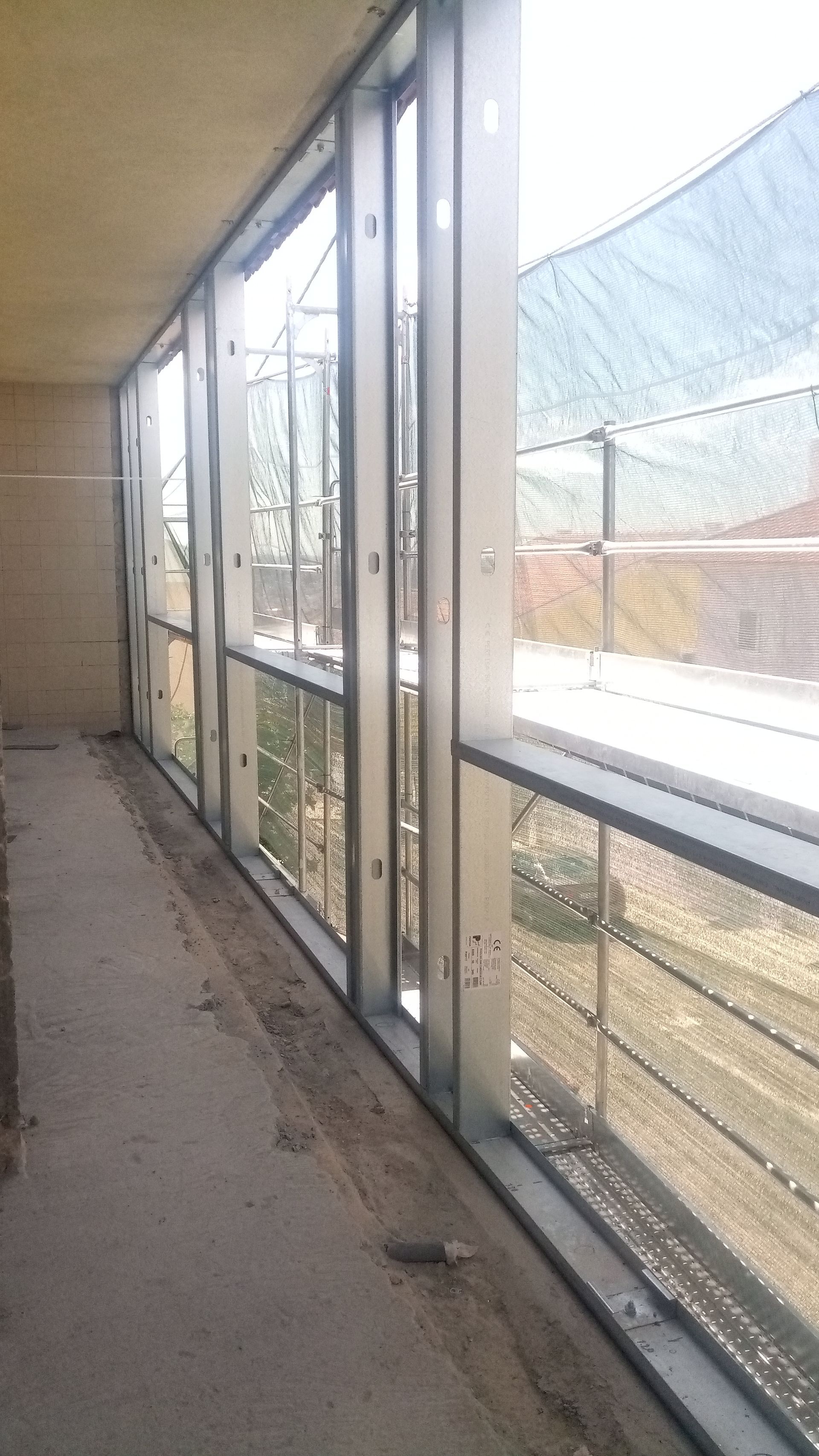 Um longo corredor com janelas de estrutura metálica, em um canteiro de obras.