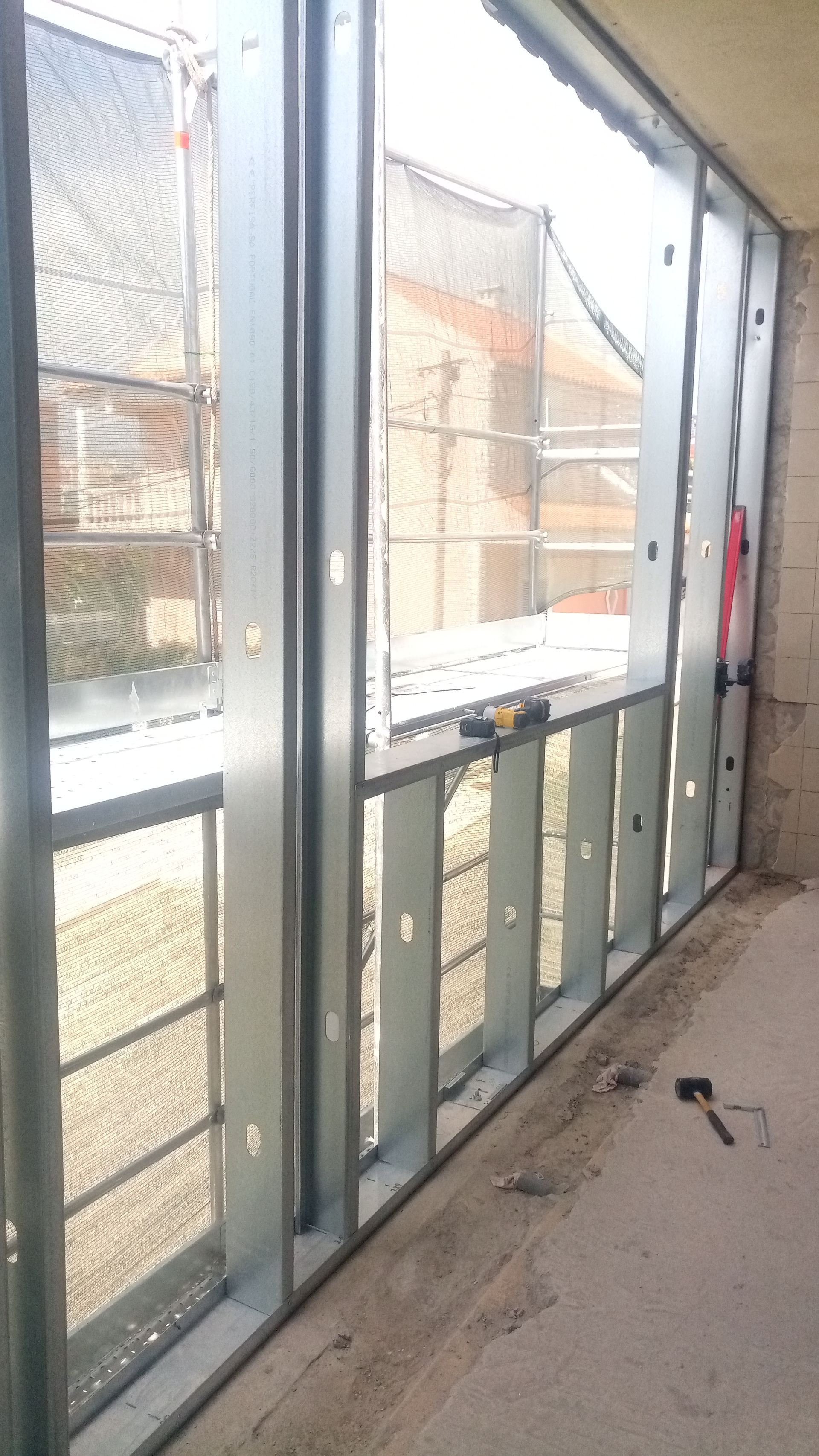Estrutura metálica de uma janela em um canteiro de obras, com vista para o exterior.