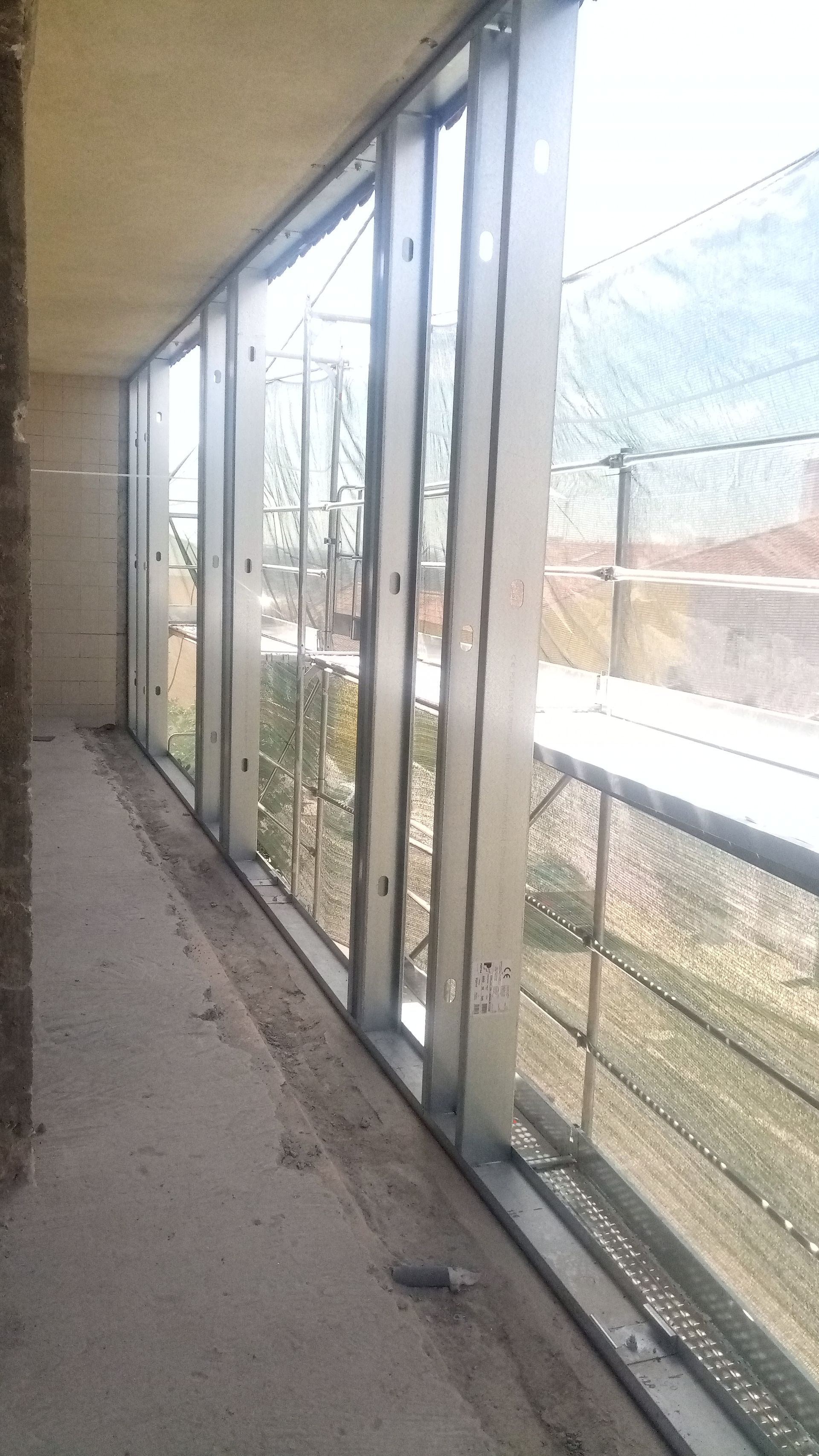 Varanda com estrutura metálica e painéis de vidro transparente, com vista para o exterior.