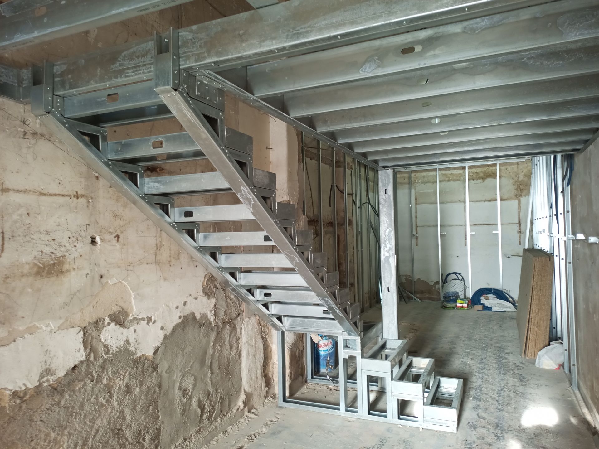 Escada metálica em construção em um cômodo com paredes e teto inacabados.