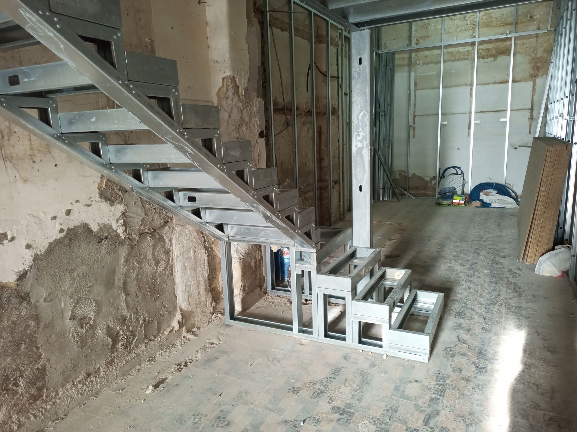 Estrutura metálica de escada em construção dentro de um prédio com paredes inacabadas.
