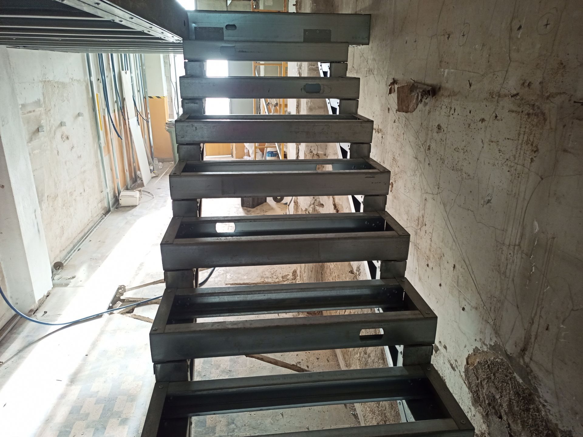 Estrutura metálica de escada em construção, encostada em uma parede de concreto.