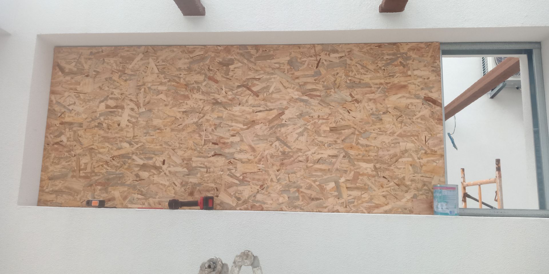 Painéis de madeira revestem uma janela, com o interior parcialmente visível e ferramentas sobre o parapeito.