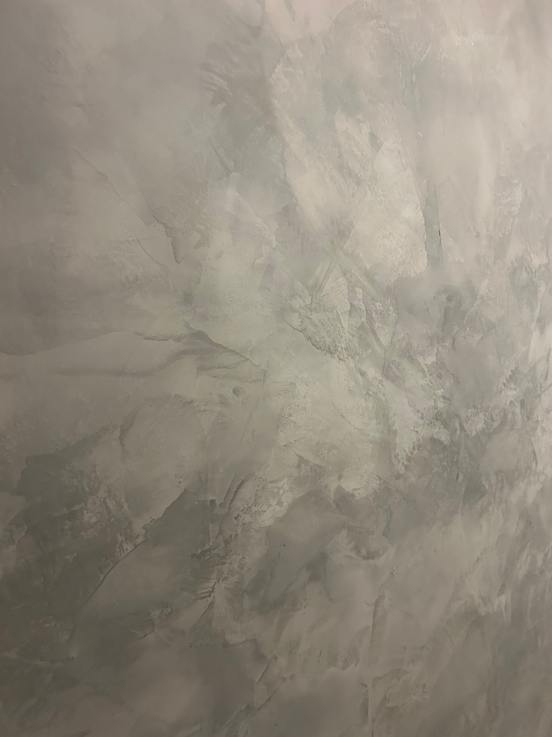 A hand uses a notched trowel to spread adhesive onto a surface in a swirled, ridged pattern.