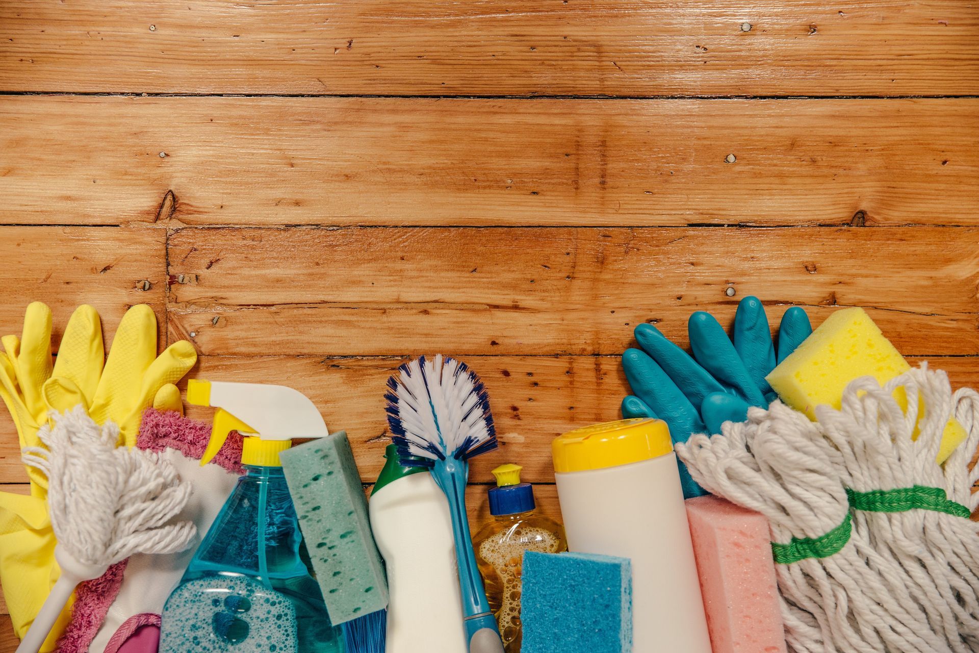 Cleaning supplies and yellow gloves arranged on a wooden surface with a scrub brush and spray bottles