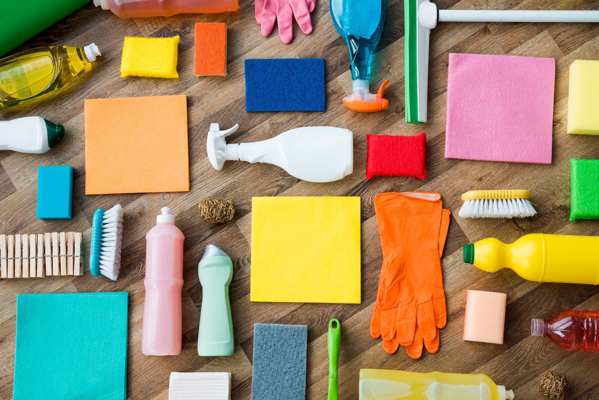 Assorted colorful cleaning supplies and sponges arranged on a wooden surface