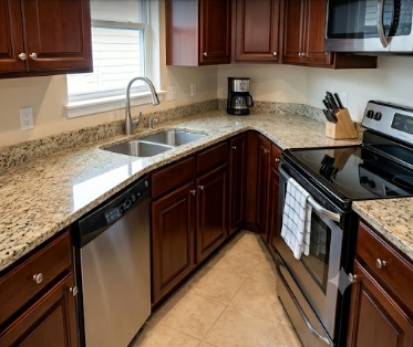 Modern kitchen corner with dark wood cabinets, granite countertops, stainless sink, and black appliances.
