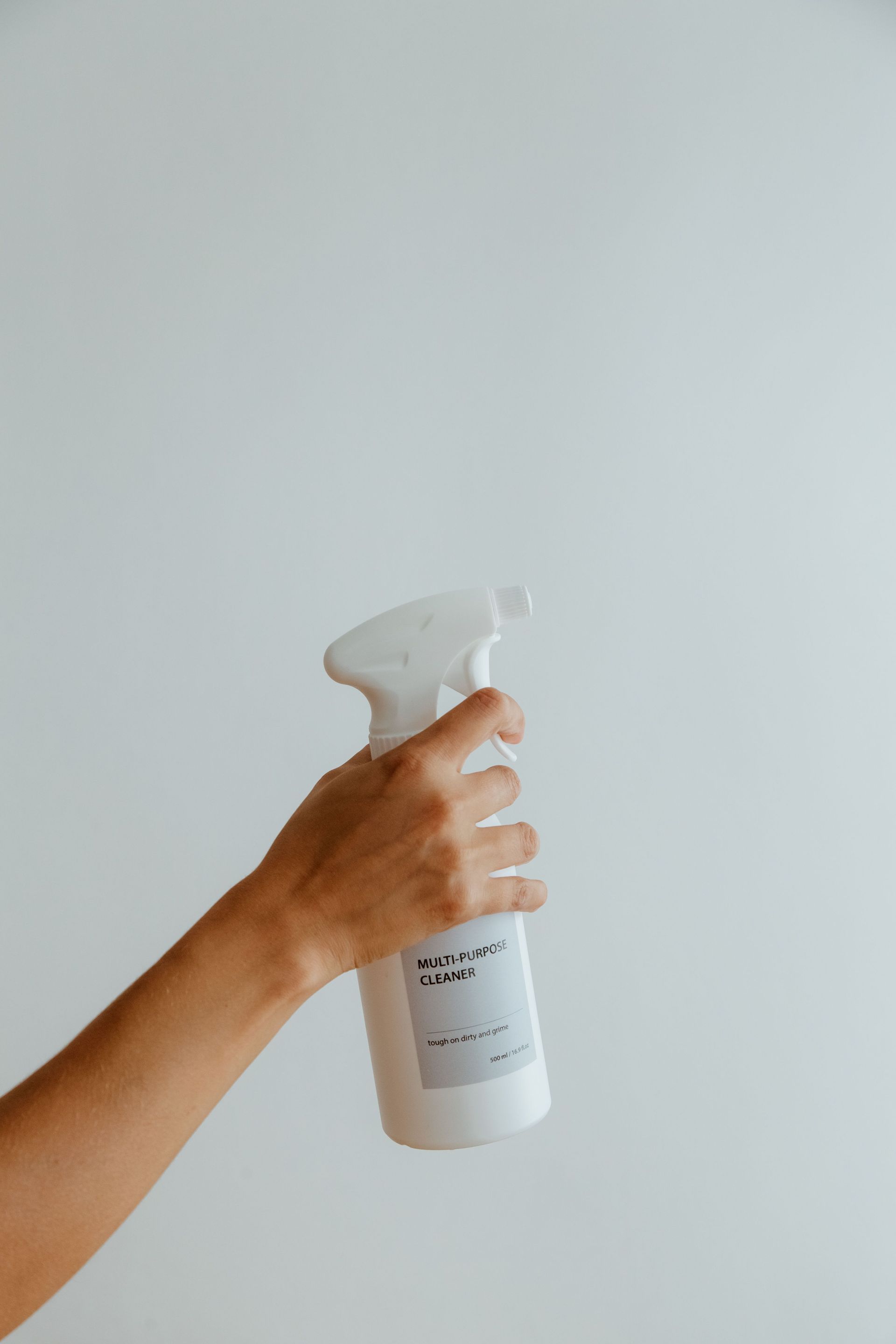 Hand holding a white spray bottle against a plain light gray background