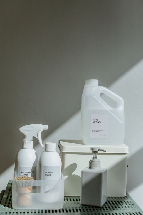 White cleaning product bottles and spray containers arranged on a shelf in soft daylight