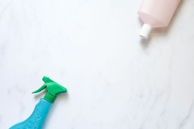 Two spray bottles on a white marble surface, one teal and one pink