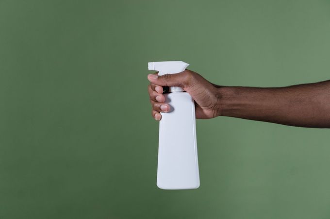 Hand holding a white spray bottle against a green background