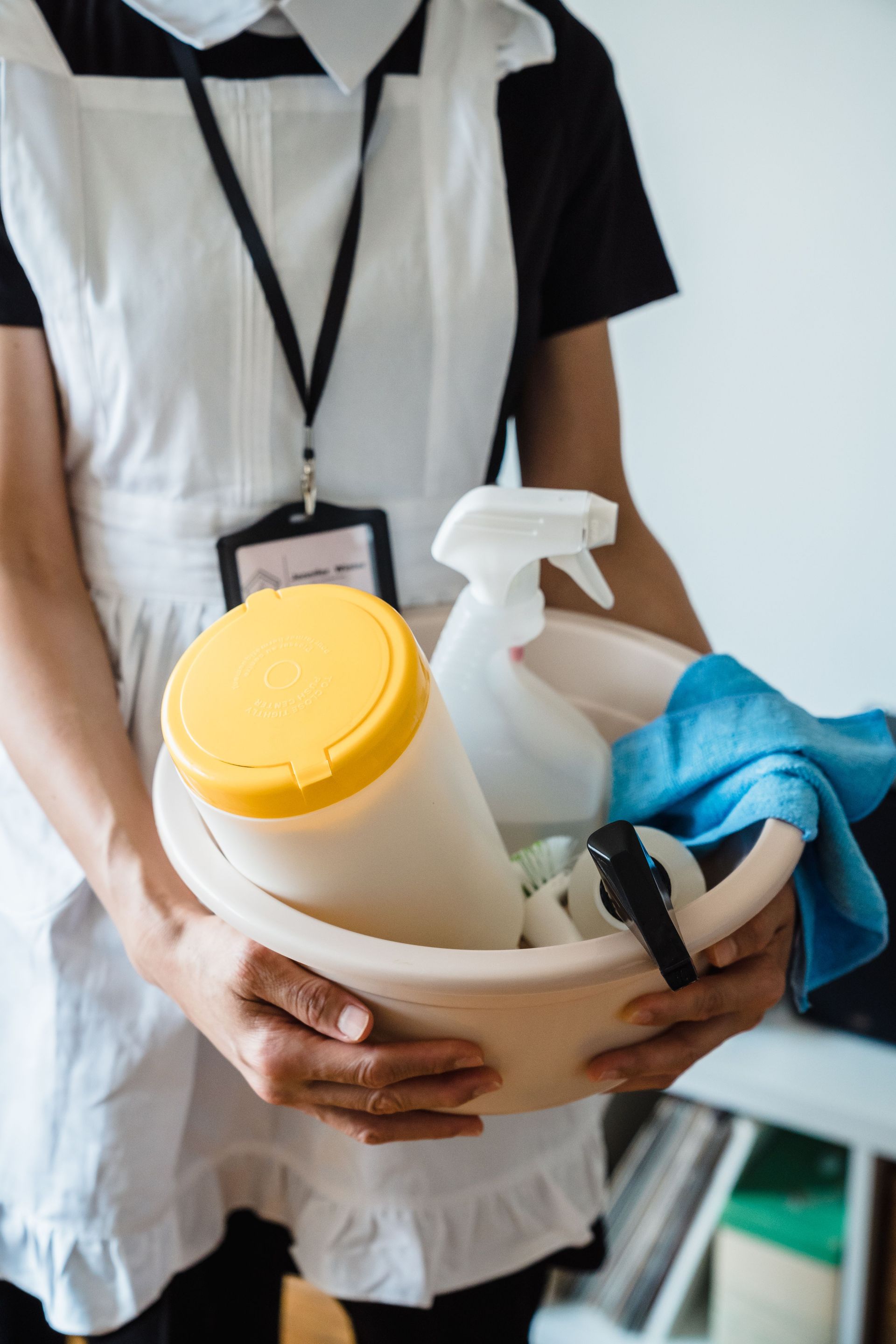 Person holding a basket of cleaning supplies, including spray bottles, cloths, and a yellow-lidded container.