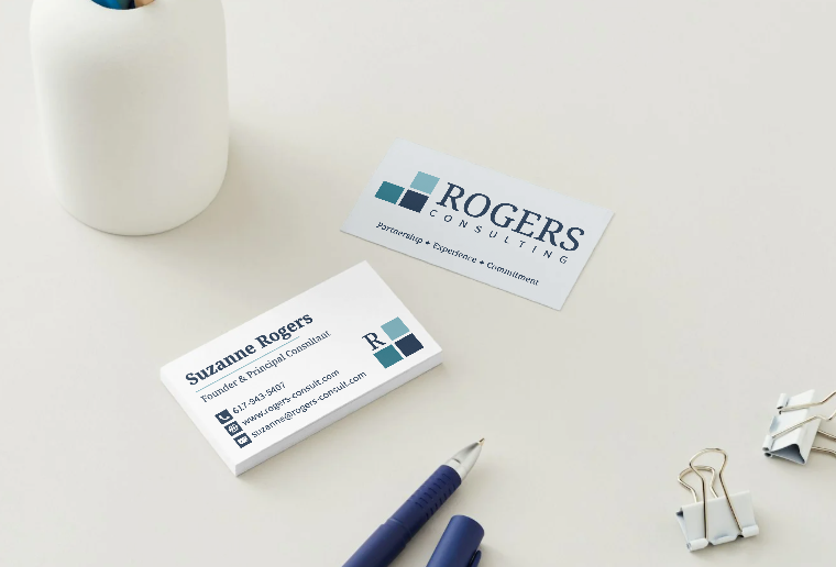 Business cards, blue pen, and binder clips on a white desk