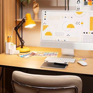 A clean workspace with a computer monitor, desk lamp, drawing tablet, and keyboard on a wooden desk.