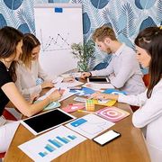 Four people sit at a table collaborating on social media marketing projects featuring app icons and data charts.