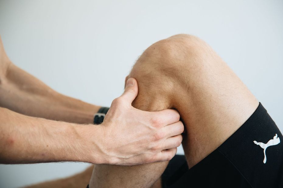 Hands massaging a bent knee, with black athletic shorts and a white Puma logo.