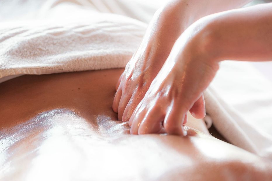 Hands massaging a person’s oiled back on a spa table