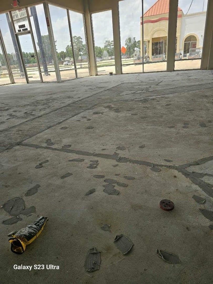 Empty room with footprints on concrete floor; a broken bottle and a bottle cap are visible.