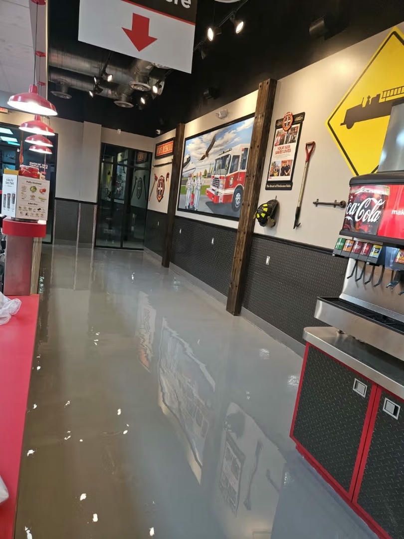 Interior of a metal building with a stained concrete floor. Large windows and door let in light.