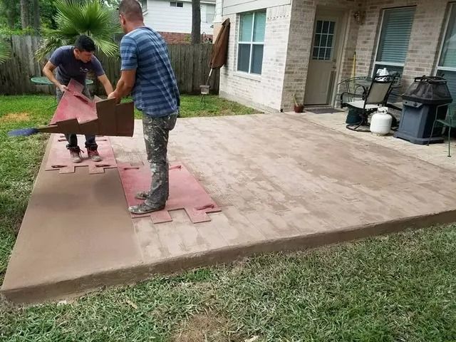 Two men installing interlocking floor tiles on a concrete patio.