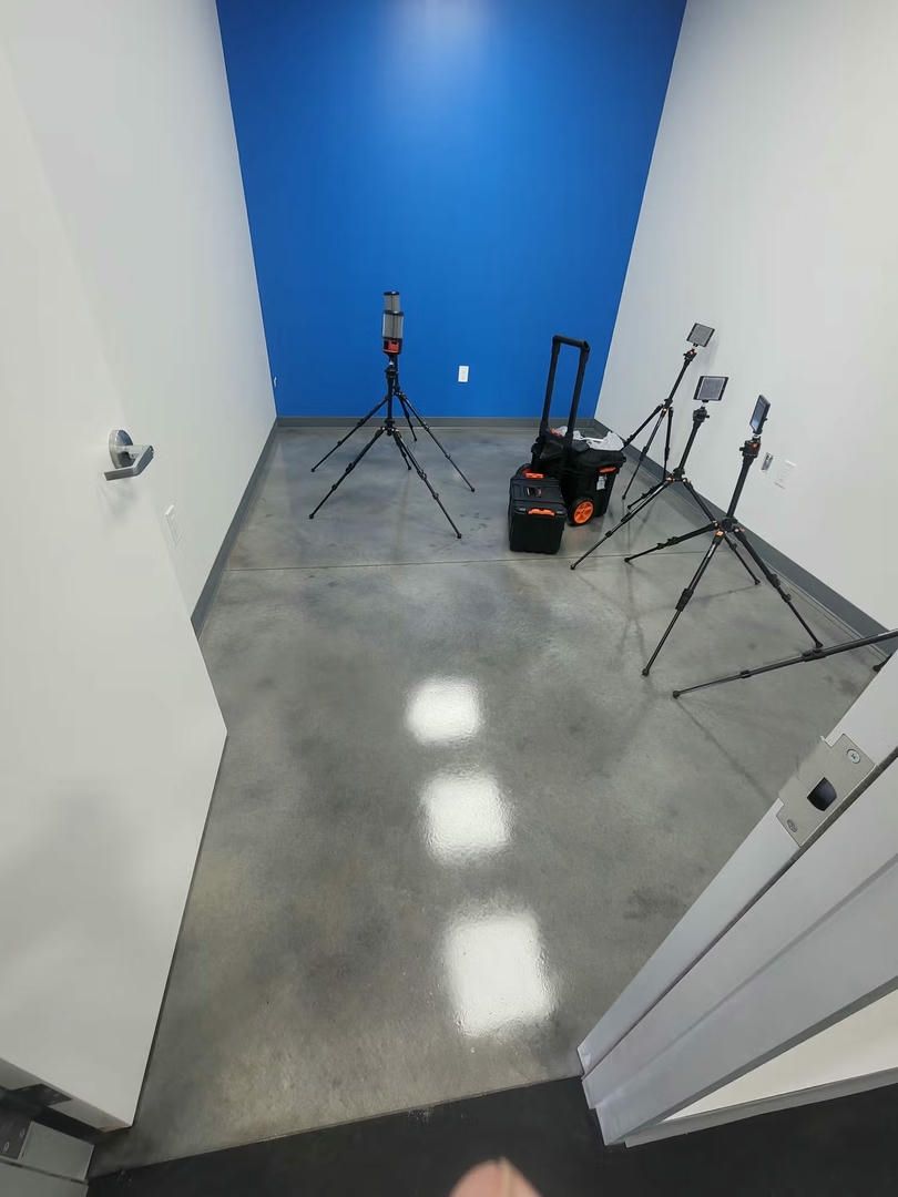 Room with a blue wall, white walls, and a gray floor. Cameras on tripods are set up.