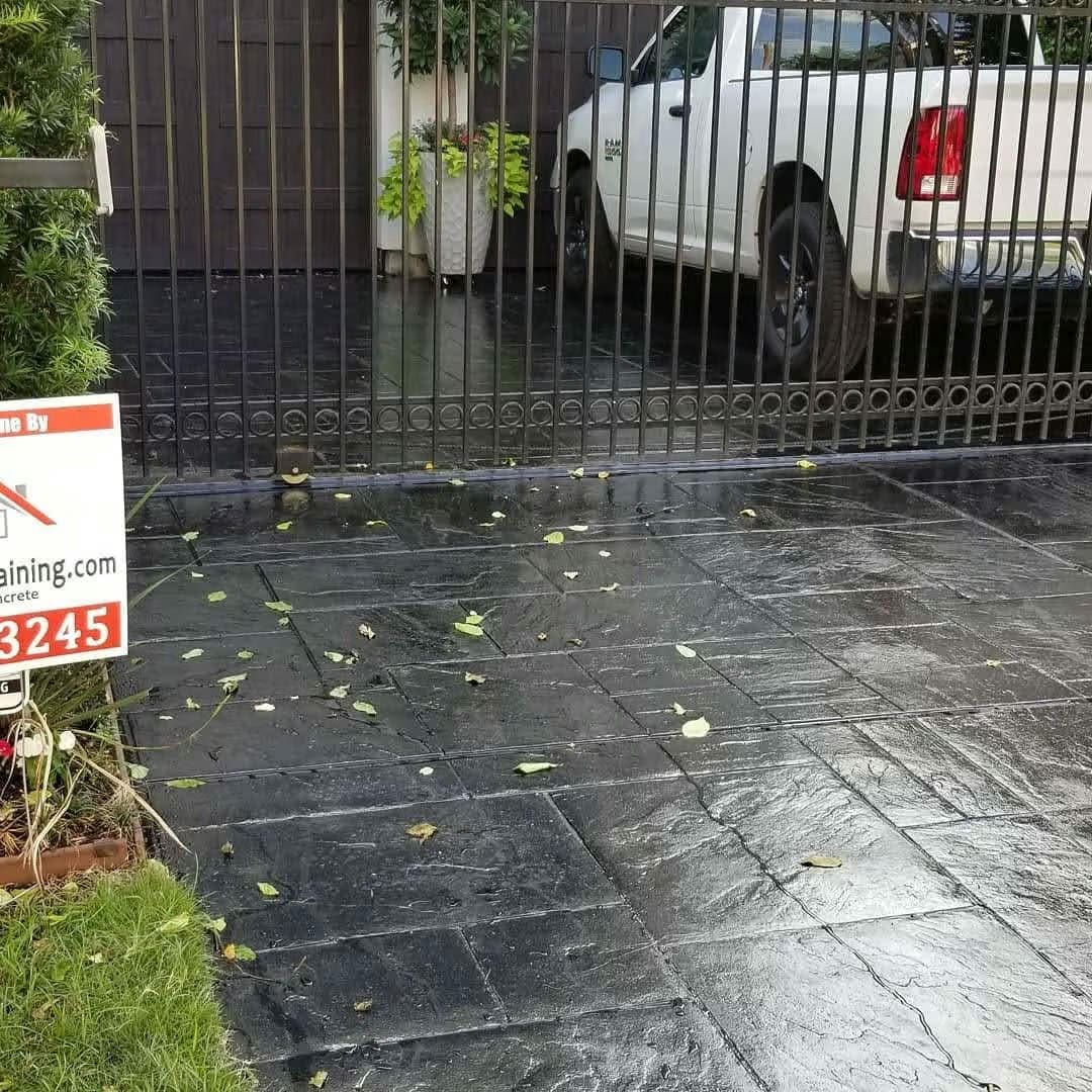 Black stamped concrete driveway with leaves, a gate, and a white pickup truck.
