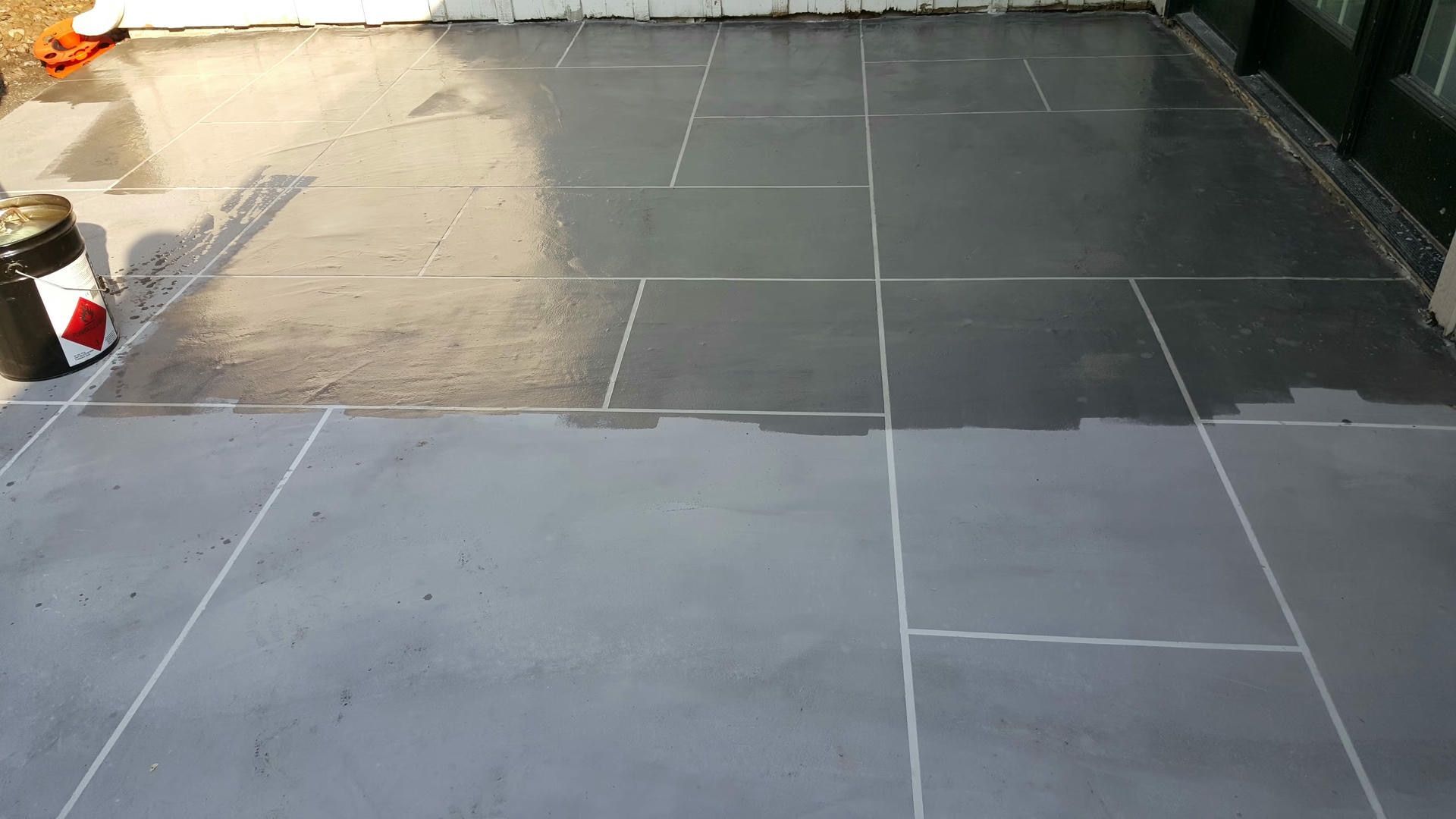 A person applying sealant to gray stone tiles on a patio. Partially sealed, with a can of sealant visible.
