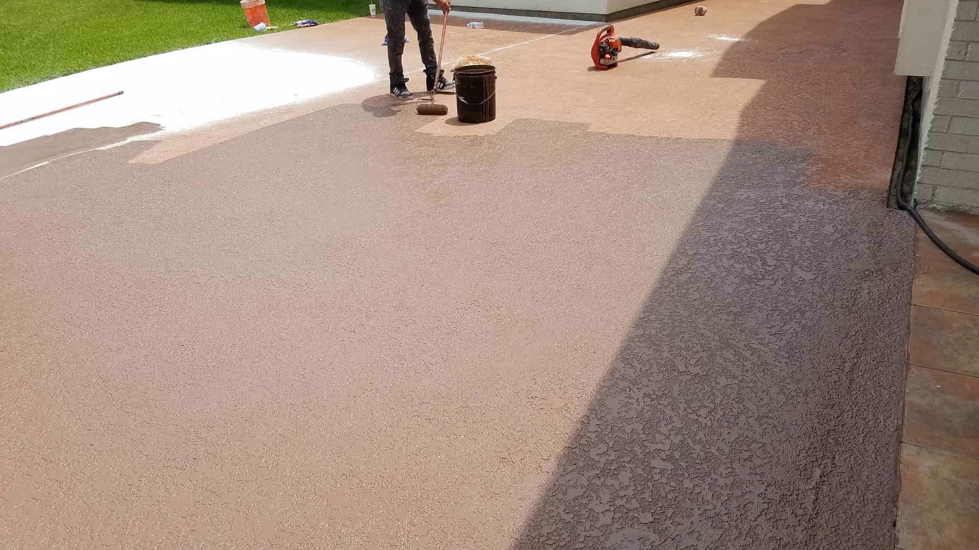 Person applying coating to a concrete patio; brown color. Tools and bucket nearby.